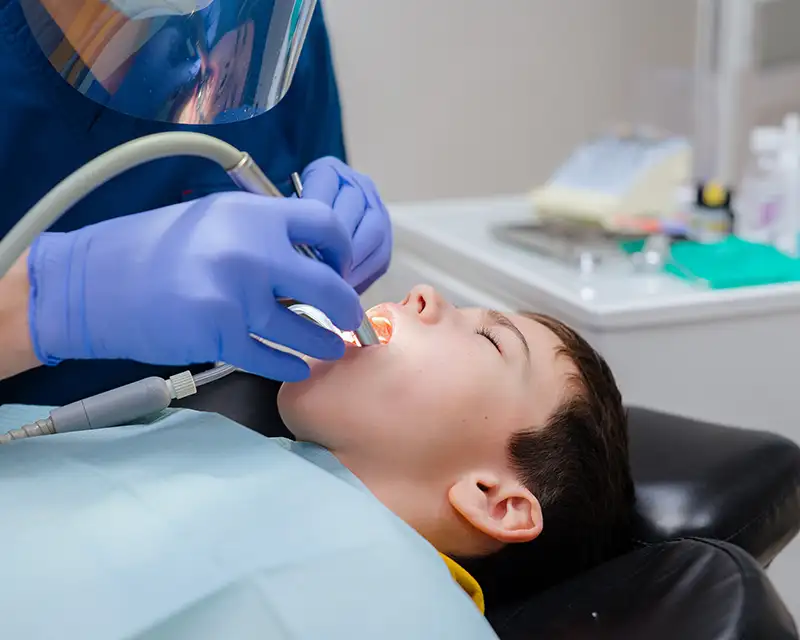 Dental professional examining patient's teeth in clinical setting wearing blue gloves.
