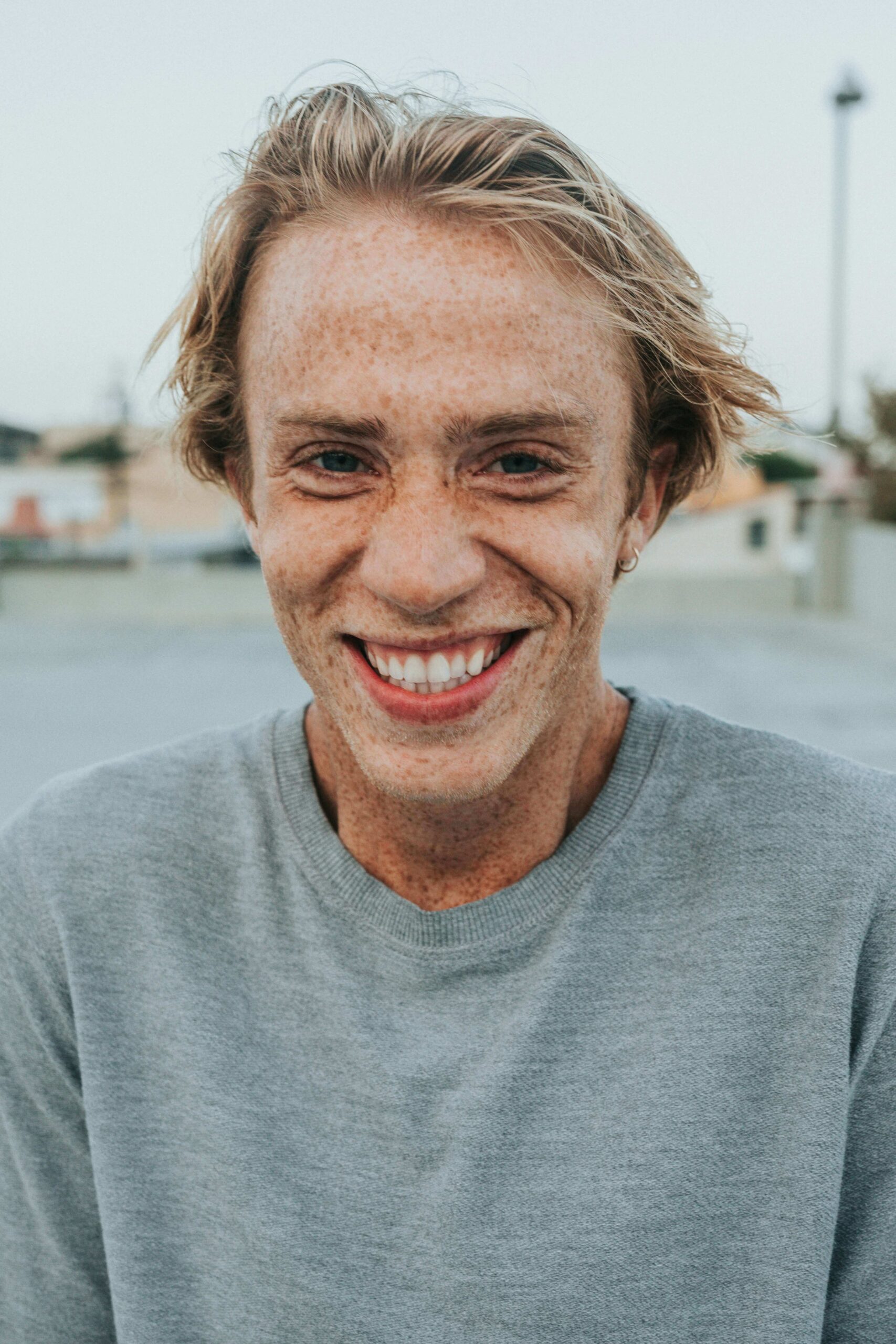 person-smiling - Vegas Smile Suite: Tozzi & Lawler Close-up of a freckled man with blond hair smiling, wearing a gray sweater, outdoors.